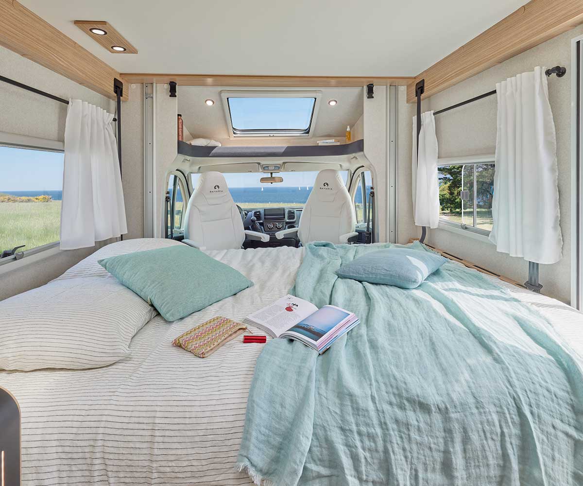 Lit de pavillon dans le salon du camping-car profilé T690D Bavaria dans un décor de bord de mer.