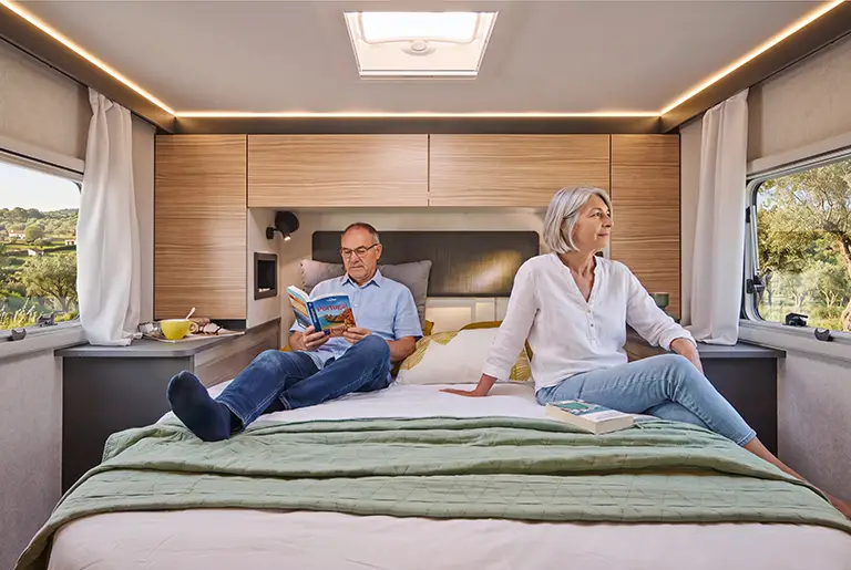 Chambre d'un camping car intégral avec grand lit et placards hauts