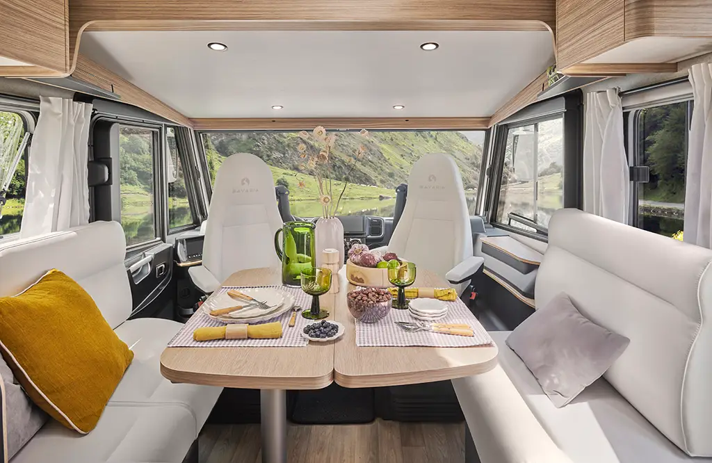 Intérieur d'un camping car intégral avec banquette en tissu clair, table en bois et sièges pivotants