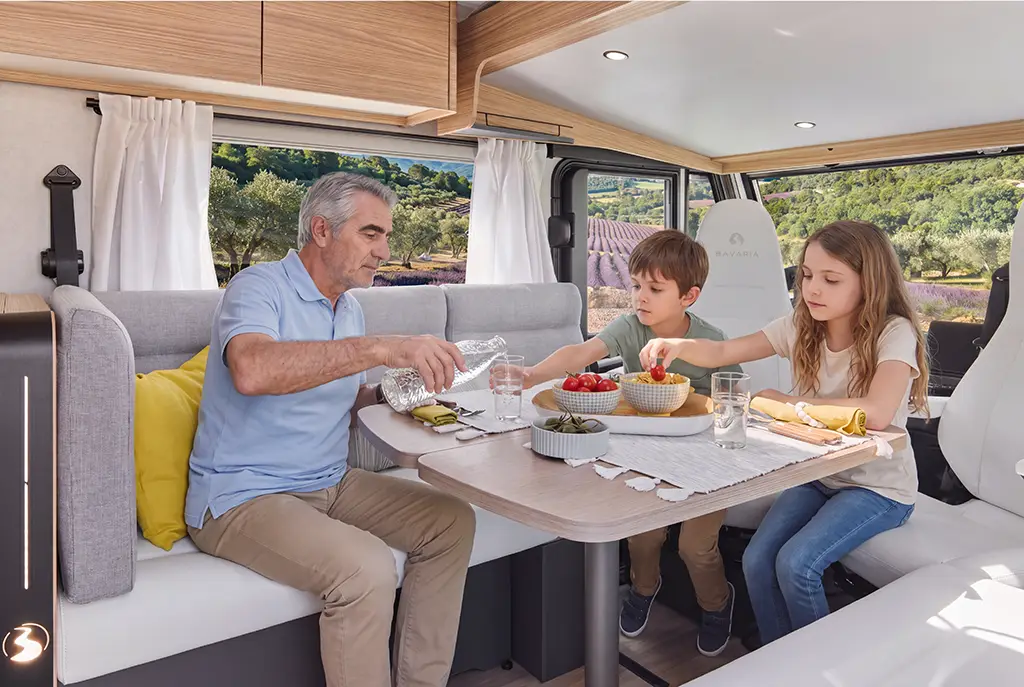 Intérieur d'un camping car intégral avec banquette en tissu clair, table en bois et sièges pivotants