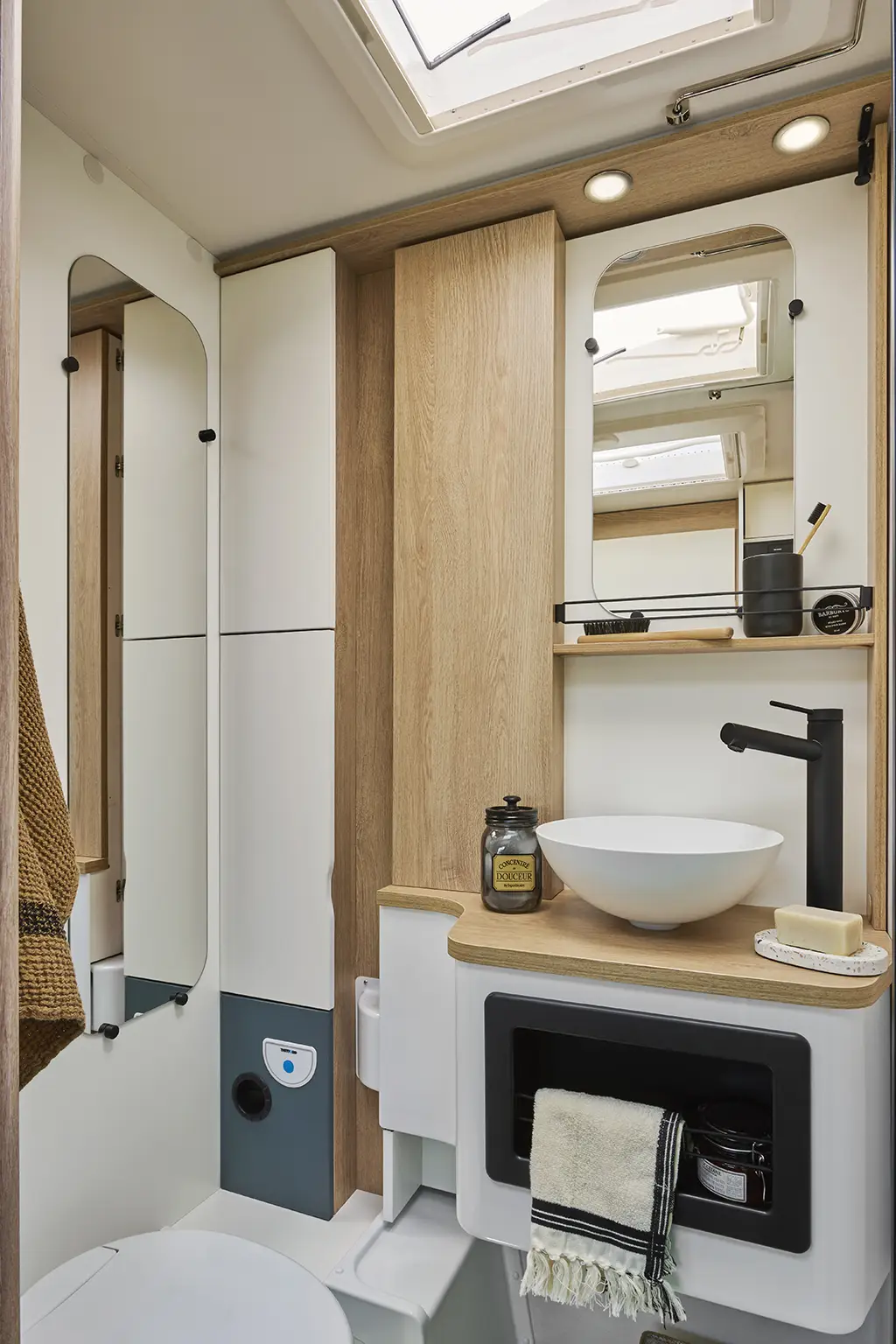 Salle de bain d'un camping car profilé étroit avec toilettes, lavabo et miroir