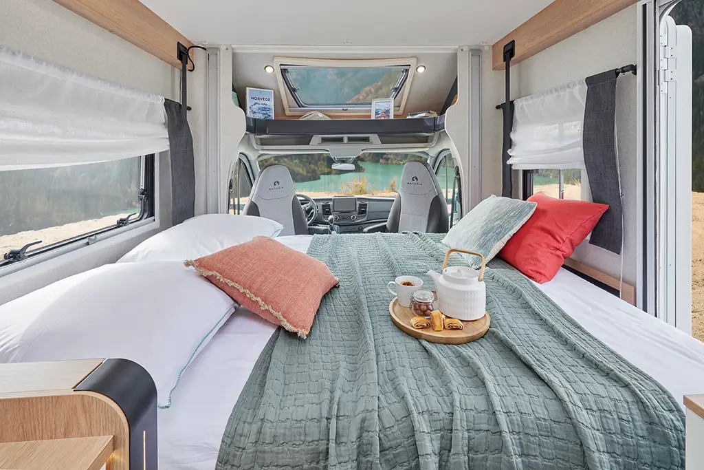Chambre d'un camping car profilé étroit avec lit transversal et sièges pivotants