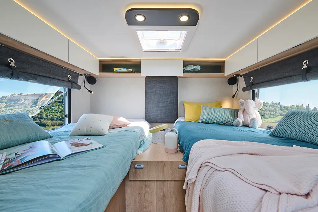 Chambre d'un camping car profilé étroit avec lits jumeaux et rangements haut