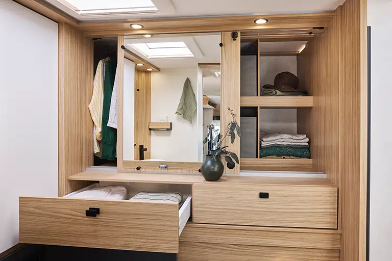 Dressing d'un camping car profilé avec placards et tiroirs en bois clair et miroir.