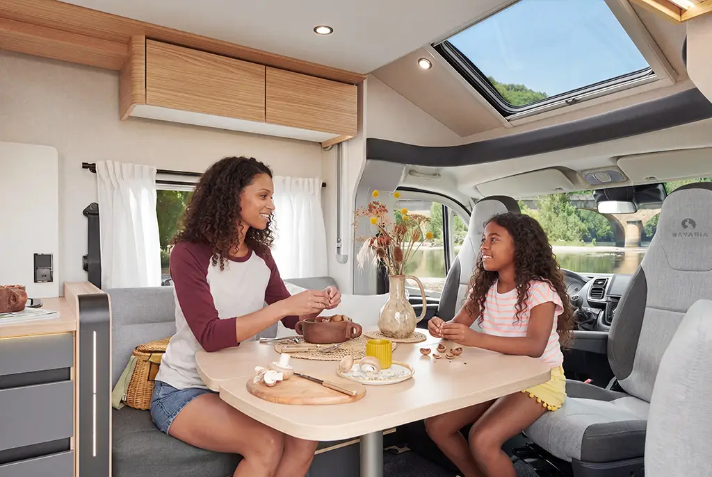 Intérieur d'un camping car profilé avec banquette en tissu gris, table en bois clair et sièges pivotants