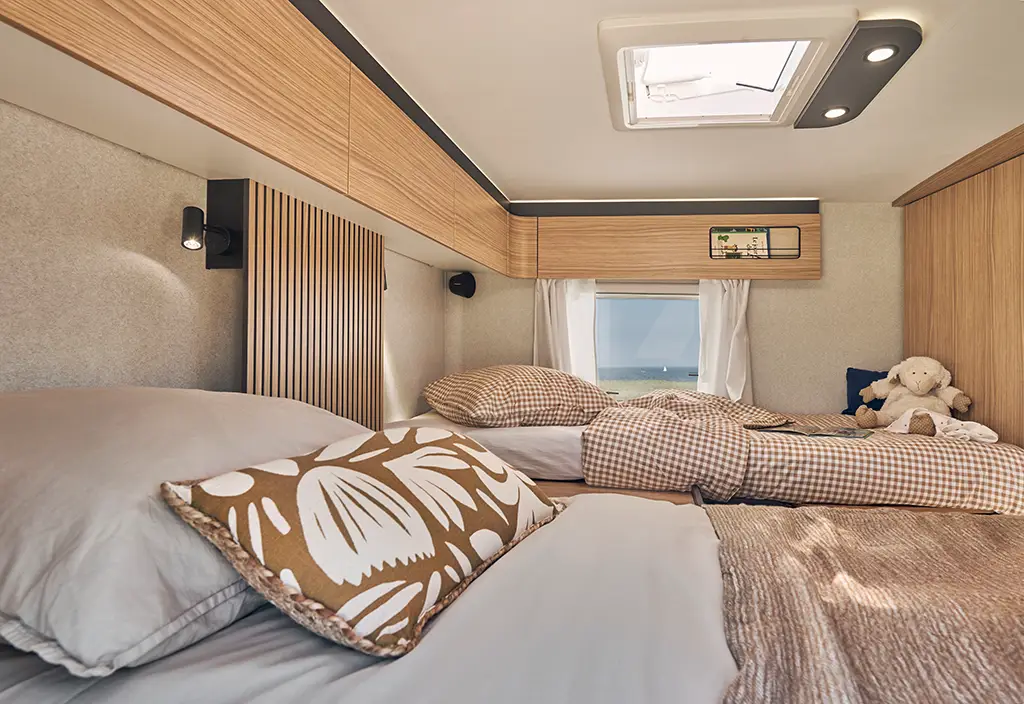 Chambre d'un camping car profilé avec lits jumeaux et rangements hauts en bois
