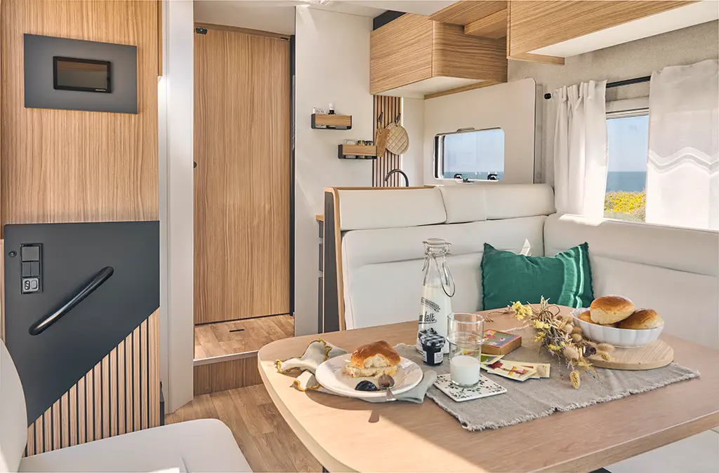 Salon d'un camping car profilé avec banquette en tissu clair, table en bois et rangements haut